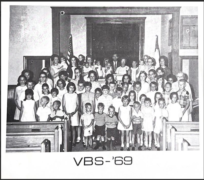 A black-and-white group photo of children and adults at Vacation Bible School in 1969, standing in rows at the front of the church