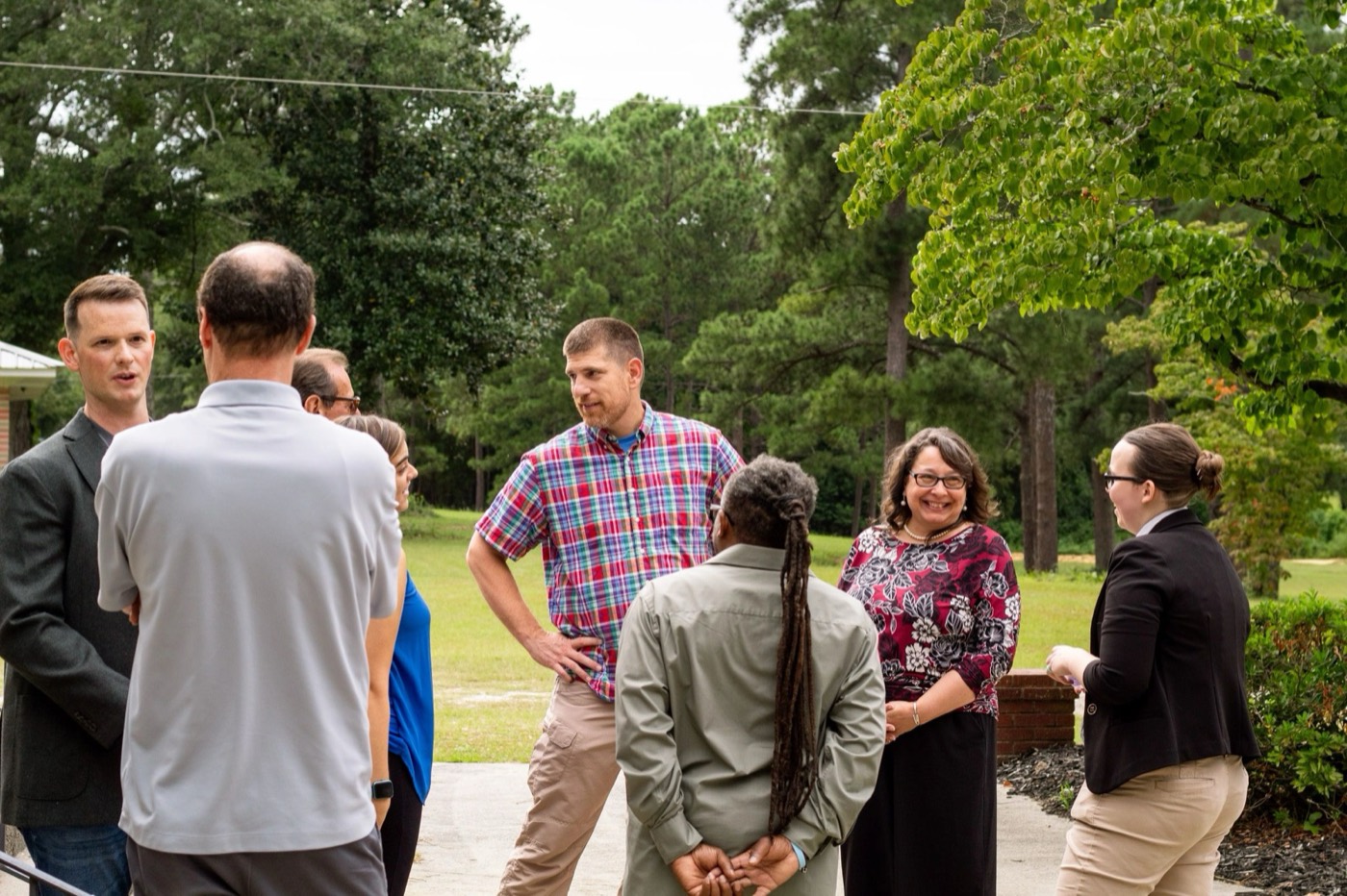 People from Hillcrest talking together on the walk outside the church, under tall pines
